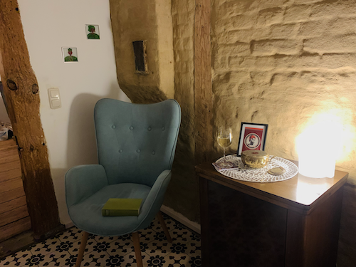 In einer Ecke steht ein Sessel. Daneben steht ein Glas Wein auf einem Holztisch. 