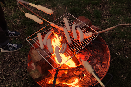 Stockbrot und Würste werden über einem Feuer gegrillt.