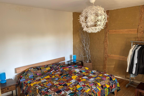 Ein Bett mit bunter Tagesdecke. Darüber eine große, runde, weiße Lampe